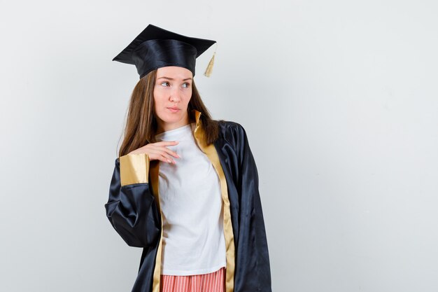 Graduada femenina posando mientras mira a otro lado en traje académico y mirando enfocado. vista frontal.
