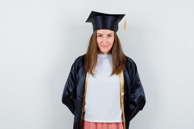 Graduada manteniendo las manos detrás de la espalda en uniforme, ropa casual y mirando avergonzado, vista frontal.