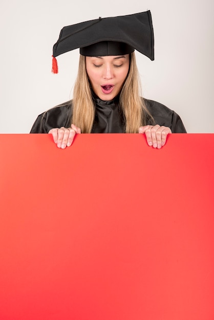 Foto gratuita graduado sorprendido sosteniendo un cartel rojo maqueta