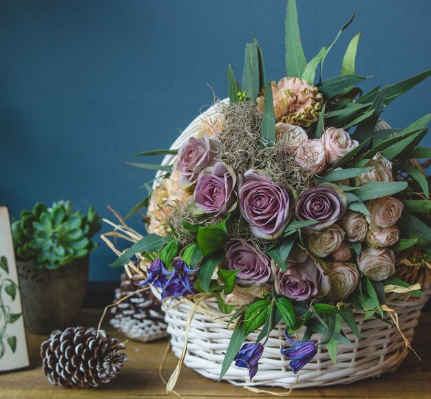 Gran canasta de flores mixtas de pie sobre una mesa con conos de navidad