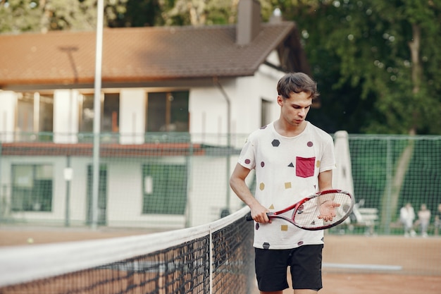 Foto gratuita ¡gran día para jugar! hombre joven alegre en camiseta. chico sosteniendo pelota y raqueta de tenis.