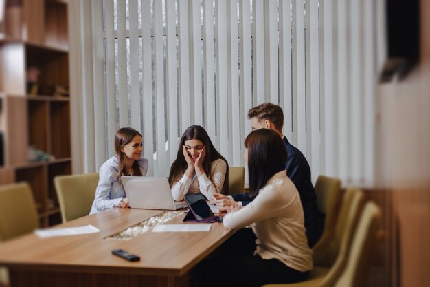 Un gran equipo de personas está trabajando en una mesa para computadoras portátiles, tabletas y papeles.