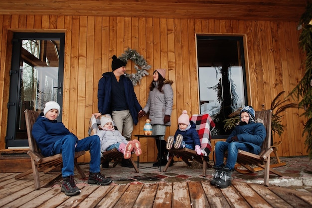 Gran familia joven con cuatro hijos en la terraza de una casa de madera en invierno