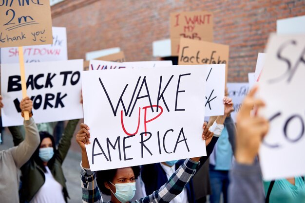 Gran grupo de manifestantes que se manifiestan en las calles de EE. UU. El foco está en la mujer negra que sostiene el cartel de 'wake up American'