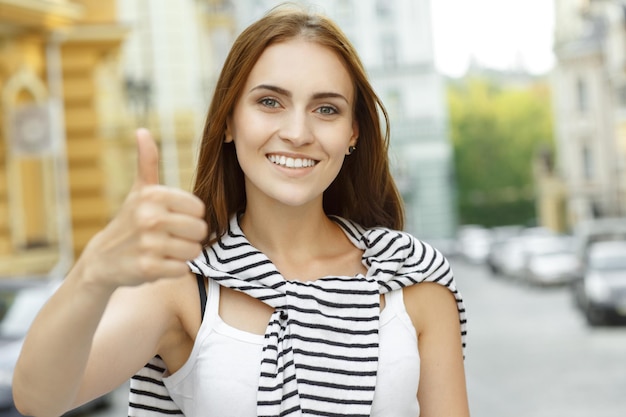 Foto gratuita gran hermosa mujer joven muestra los pulgares hacia arriba sonriendo mirando a la cámara