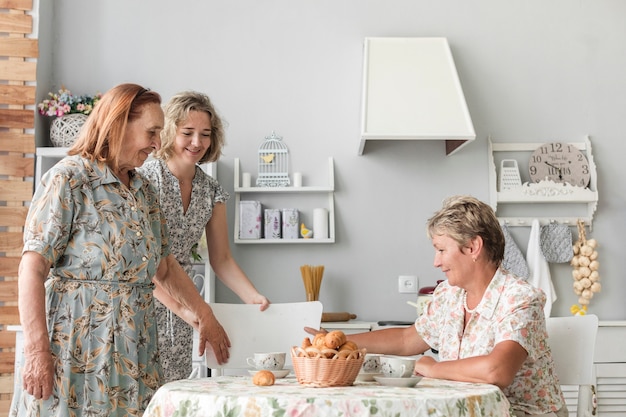 Gran hija arreglando silla para su abuelita en la cocina