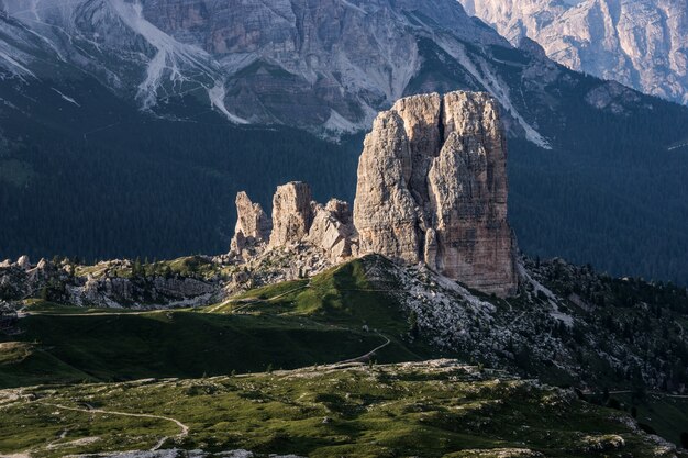 Gran roca en una colina cubierta de hierba con montañas boscosas