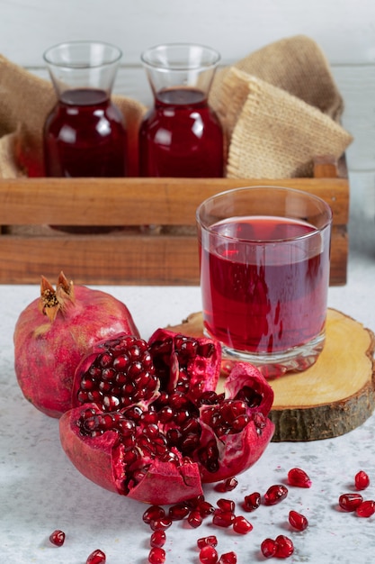 Foto gratuita granada orgánica en rodajas y entera con vasos de jugo fresco.