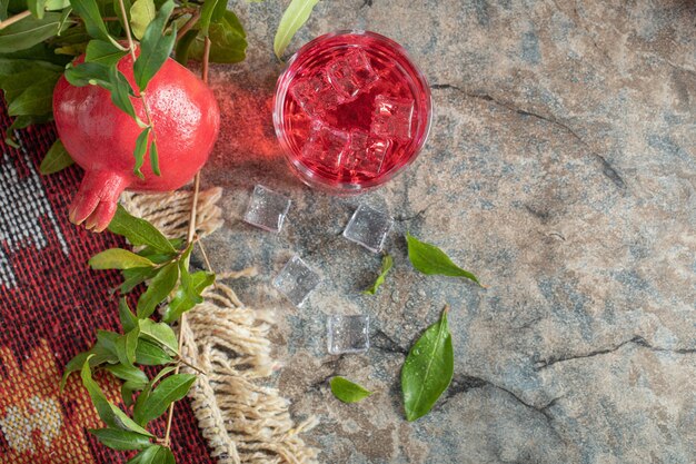 Granada y vaso de jugo sobre fondo de piedra con hojas