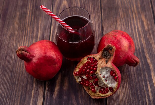 Granadas de vista lateral con un vaso de jugo y una pajita roja sobre una pared de madera