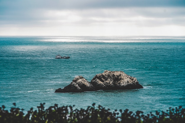 Grandes rocas en medio del mar y un guardacostas navegando a lo lejos