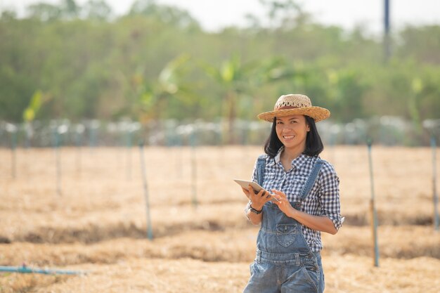 Granja inteligente. Hermoso agricultor usa tableta para controlar su granja y negocio con felicidad y sonrisa. Concepto de agricultura y negocios. El agricultor o el agrónomo examinan preparar una parcela para cultivar hortalizas.