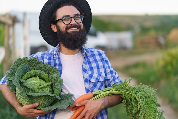 Granjero abrazando verduras frescas con manos sonriendo sosteniendo zanahorias y repollo. Preparándose para la entrega ecológica orgánica