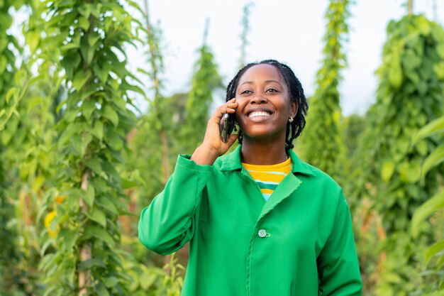 Granjero africano alegre hablando por teléfono mientras trabaja en el campo