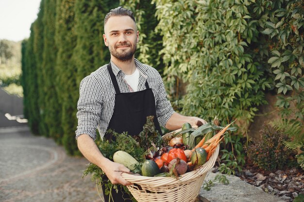 Granjero alegre con verduras orgánicas en el jardín. Vegetales orgánicos mixtos en canasta de mimbre.