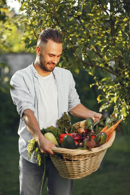 Granjero alegre con verduras orgánicas en el jardín. Vegetales orgánicos mixtos en canasta de mimbre.