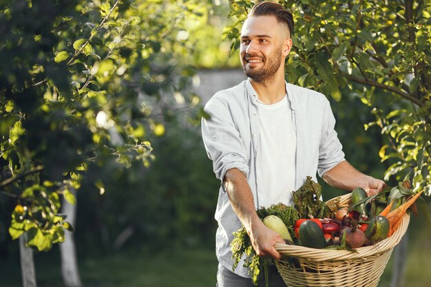 Granjero alegre con verduras orgánicas en el jardín. Vegetales orgánicos mixtos en canasta de mimbre.