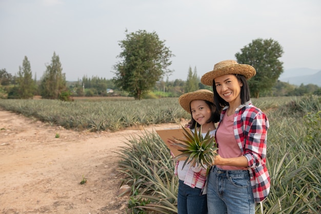 Granjero asiático hace que madre e hija vean el crecimiento de la piña en la granja y guarden los datos en la lista de verificación del granjero en su portapapeles