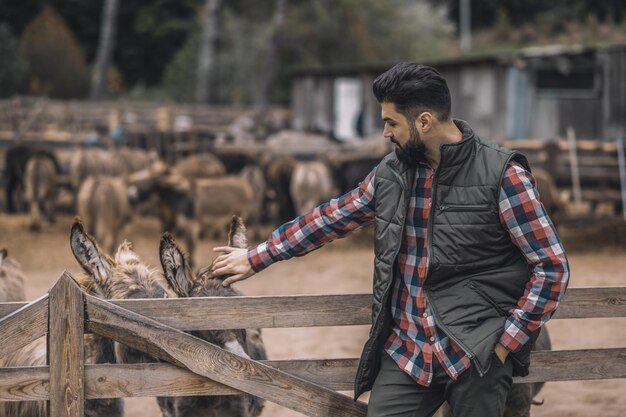 Un granjero con chaleco negro y camisa a cuadros de pie cerca del corral de ganado.