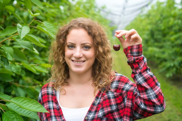 Granjero de mujer hermosa con cereza en huerto verde