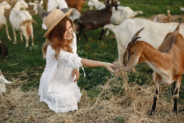 Granjero de niña con cabra blanca. Mujer y pasto verde de cabra pequeña. Granja ecológica. Concepto de granja y agricultura. Animales del pueblo. Niña juega linda cabra. F