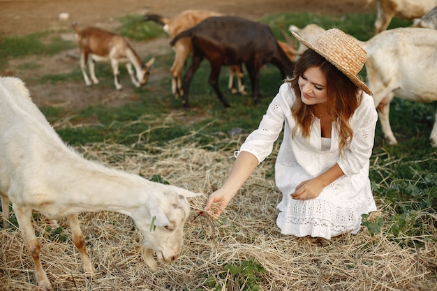 Granjero de niña con cabra blanca. Mujer y pasto verde de cabra pequeña. Granja ecológica. Concepto de granja y agricultura. Animales del pueblo. Niña juega linda cabra. F