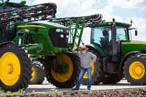 Foto gratuita granjero profesional con un tractor moderno, combinar en un campo a la luz del sol en el trabajo. colores veraniegos seguros y brillantes. agricultura, exposición, maquinaria, producción vegetal. hombre mayor cerca de su máquina.