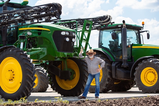 Granjero profesional con un tractor moderno, combinar en un campo a la luz del sol en el trabajo. Colores veraniegos seguros y brillantes. Agricultura, exposición, maquinaria, producción vegetal. Hombre mayor cerca de su máquina.