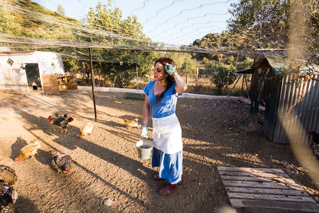 Granjero de sexo femenino agotado que alimenta el pollo en el campo