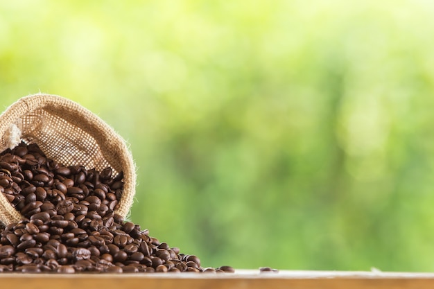 Grano de café en el saco en la mesa de madera contra el fondo verde de desenfoque de grunge