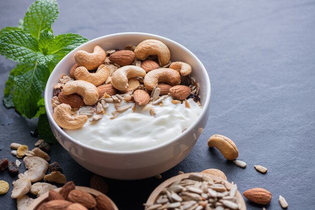 Granola casera o muesli, tazón de granola de avena con yogur, almendras, anacardos, menta y nueces en el tablero de roca negra para un desayuno saludable, copie el espacio. Concepto de menú de desayuno saludable.