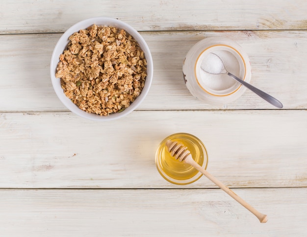 Granola con semillas de calabaza; Leche en polvo en jarra y miel en mesa de madera
