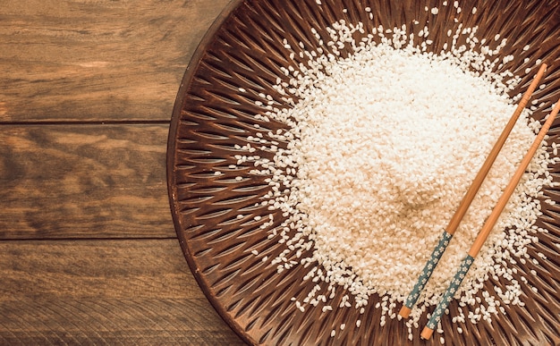 Granos de arroz blanco y palillos en la bandeja sobre el fondo de madera