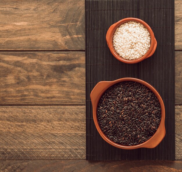 Granos de arroz marrón y blanco en el recipiente en la bandeja sobre la mesa de madera