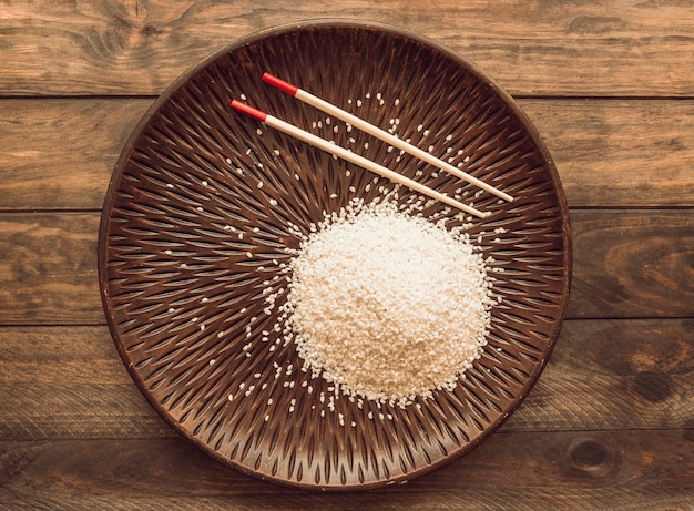 Granos de arroz en placa de madera con palillos sobre el fondo de madera