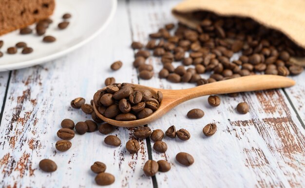 Granos de café en la cuchara de madera y sacos de cáñamo en una mesa de madera blanca.