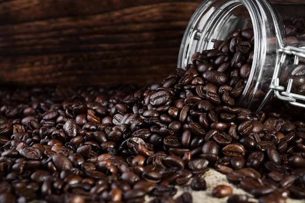 Los granos de café fragantes se dispersan de un frasco sobre un fondo rústico de mesa Enfoque selectivo de primer plano Copiar banner espacial