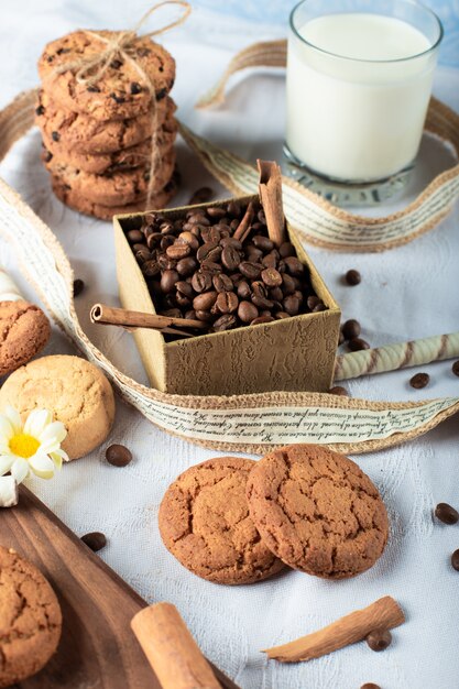 Granos de café y galletas de mantequilla con un vaso de leche sobre un mantel azul