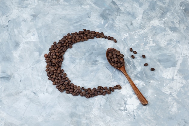 Granos de café laicos planos en cuchara de madera sobre fondo de yeso gris. horizontal