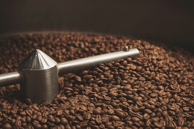 Granos de café oscuro, aromático, chocolate recién horneado y amanecer fresco caliente dentro de la mejor máquina tostadora profesional