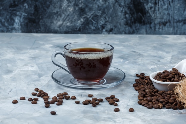 Granos de café de primer plano en jarra de porcelana blanca con taza de café sobre fondo de mármol azul oscuro y azul claro. horizontal