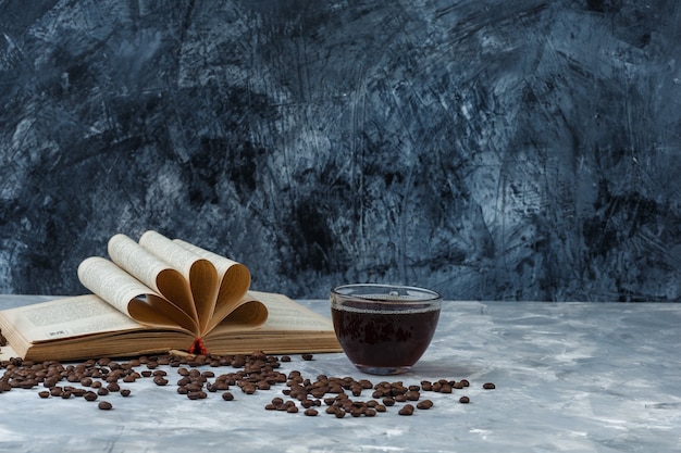 Granos de café de primer plano, taza de café con libro sobre fondo de mármol azul claro y oscuro. horizontal