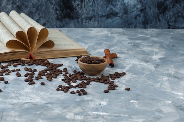 Granos de café de primer plano en un tazón de madera con libro, canela sobre fondo de mármol azul claro y oscuro. horizontal