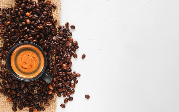 Granos de café recién tostados y una taza de café expreso caliente con espuma, ubicados a la izquierda sobre una amplia superficie blanca de hormigón