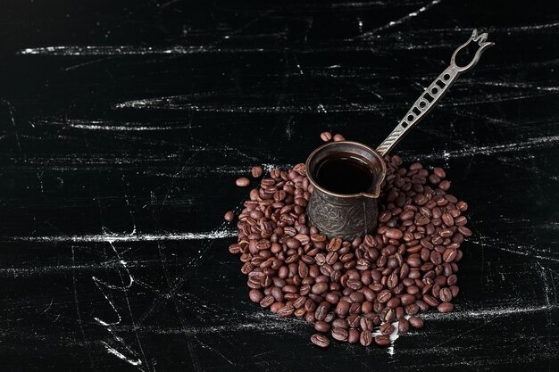 Granos de café sobre fondo negro con una olla metálica.