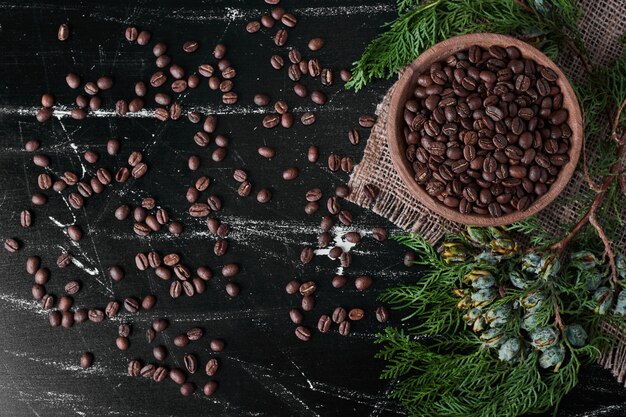 Granos de café sobre fondo negro en la taza de madera.