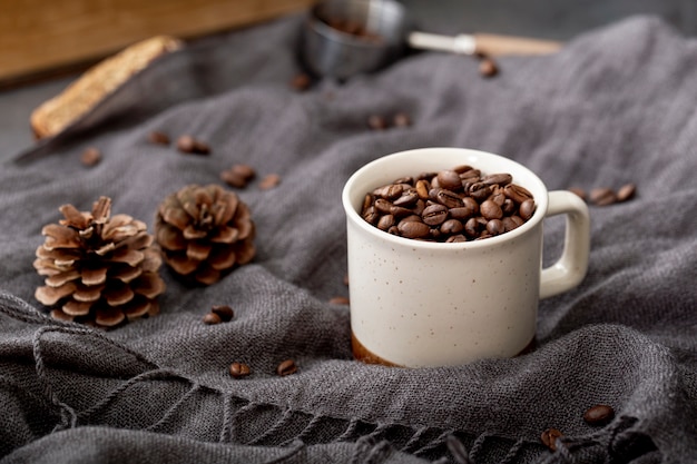 Granos de café en una taza blanca sobre una bufanda gris