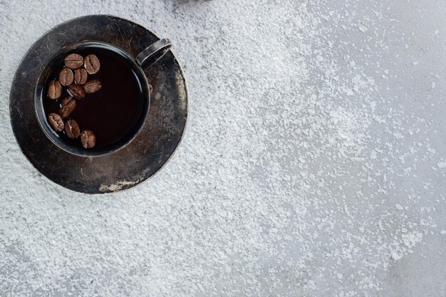 Granos de café en una taza de café con coco en polvo sobre una mesa de mármol.