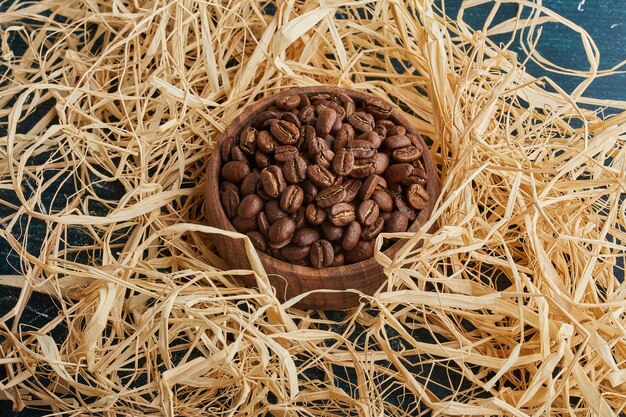 Granos de café en una taza de madera sobre la hierba seca.