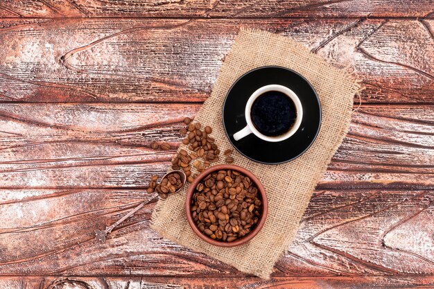 Granos de café en un tazón de cerámica con taza de café sobre superficie de madera